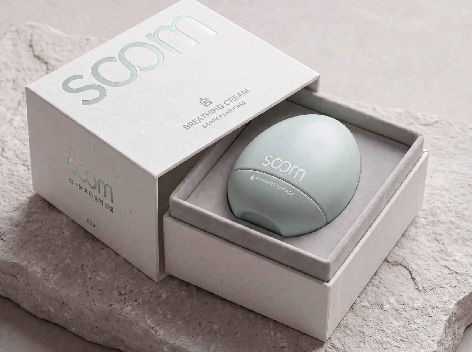 The Breathing Cream drawer box slid open on a pale stone slab, the pebble compact in a grey felt bed