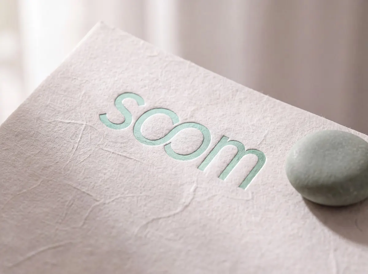 The soom wordmark in mint, pressed into textured paper, a smooth green stone beside it